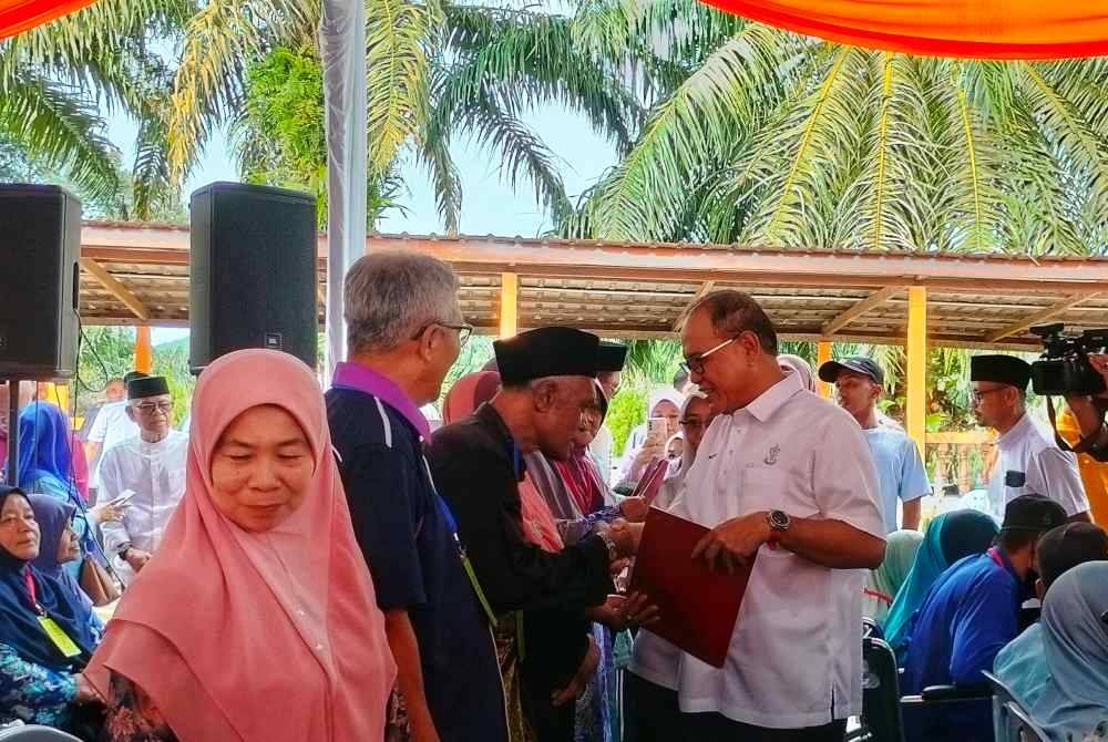 Wan Rosdy (Kanan) ketika menyerahkan suratan hak milik kepada peneroka.