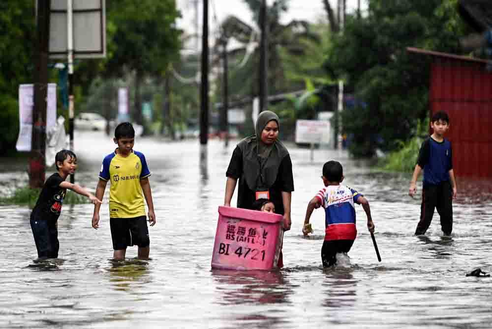 Penduduk meredah banjir selepas kawasan berkenaan dinaiki air berikutan hujan lebat sejak malam tadi ketika tinjauan Bernama di Jalan Kamaruddin pada Selasa. Foto Bernama