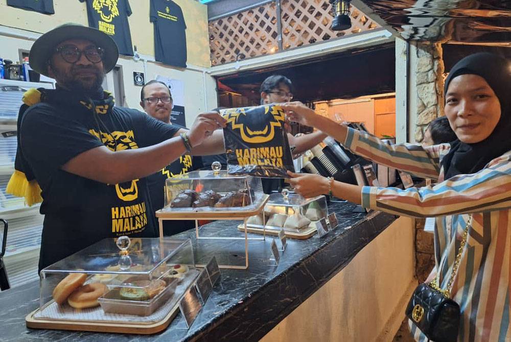 Khairun (kiri) menyerahkan baju T Harimau Malaya kepada seorang pelanggan di Kafe Kopi & Pantun, Seksyen 10, Shah Alam.