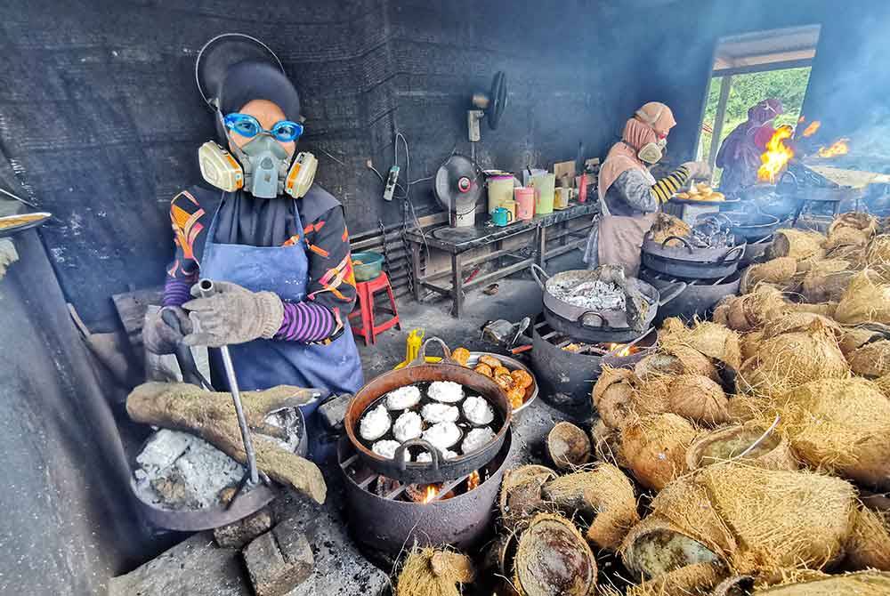 Raja Nurul Wahida (kiri) menyediakan kuih beker nyior di gerai yang beroperasi di Kampung Padang Tengir, Manir.