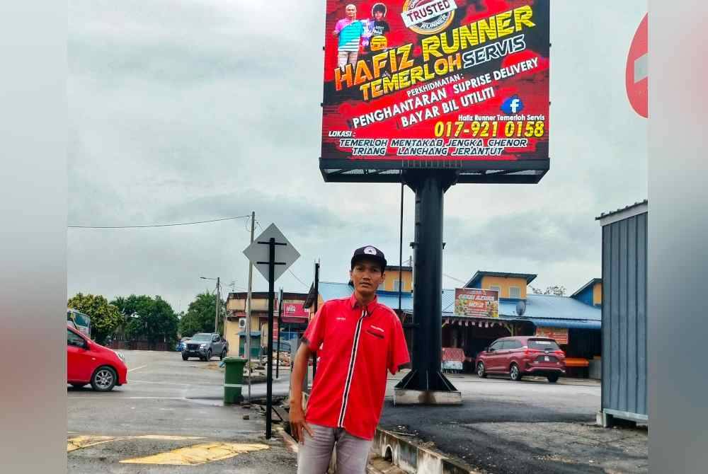 Muhammad Hafiz yang kudung tangan kiri akibat kemalangan pada 2008 di hadapan papan digital yang memaparkan khidmatnya