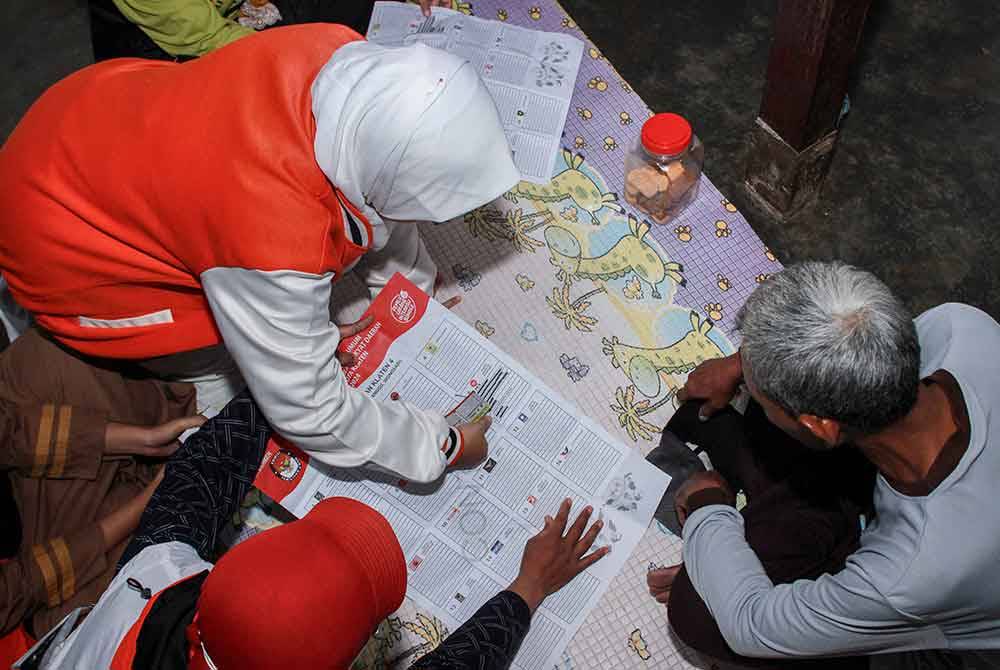 Lingga (kiri) menerangkan proses pengundian kepada penduduk tempatan di bandar Klaten. - AFP