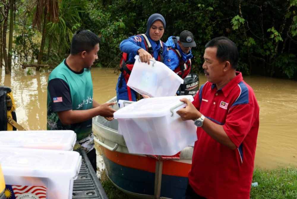 Anggota APM dibantu penduduk kampung mengangkat kit makanan untuk diserahkan kepada mangsa banjir di Kampung Besut pada Khamis. Foto Bernama