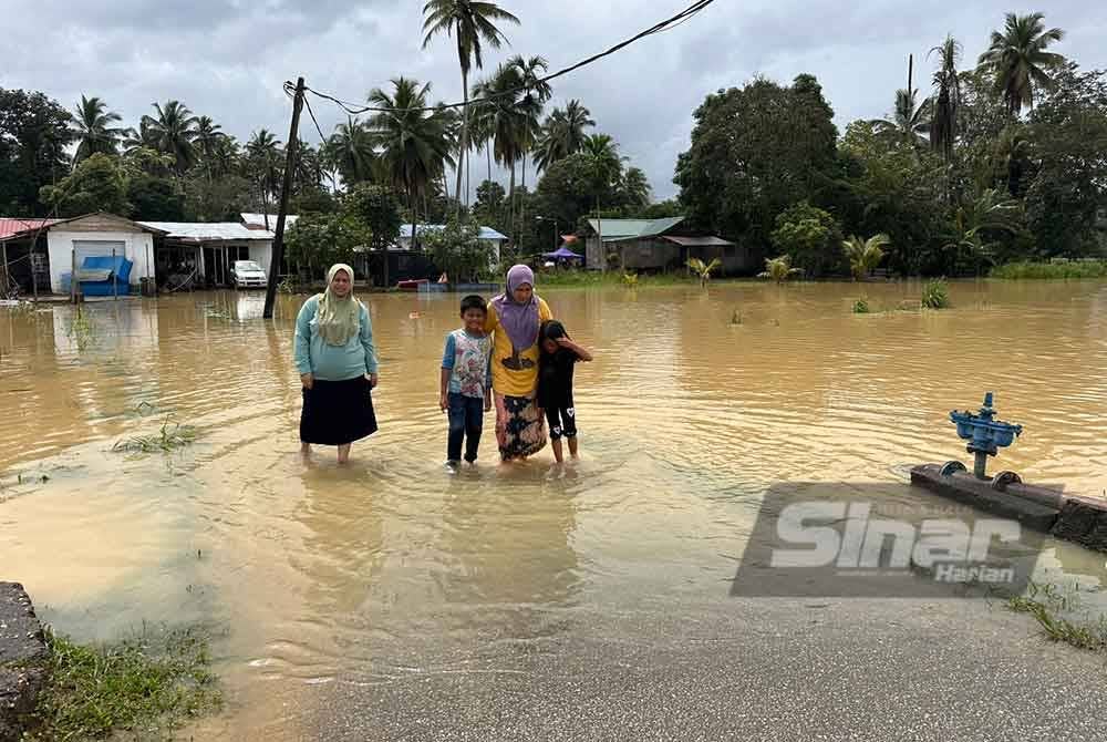 Nurul Aida (kiri) dan Azlina (dua dari kanan) bersama-sama anaknya mengharungi air untuk keluar dari rumah mereka.
