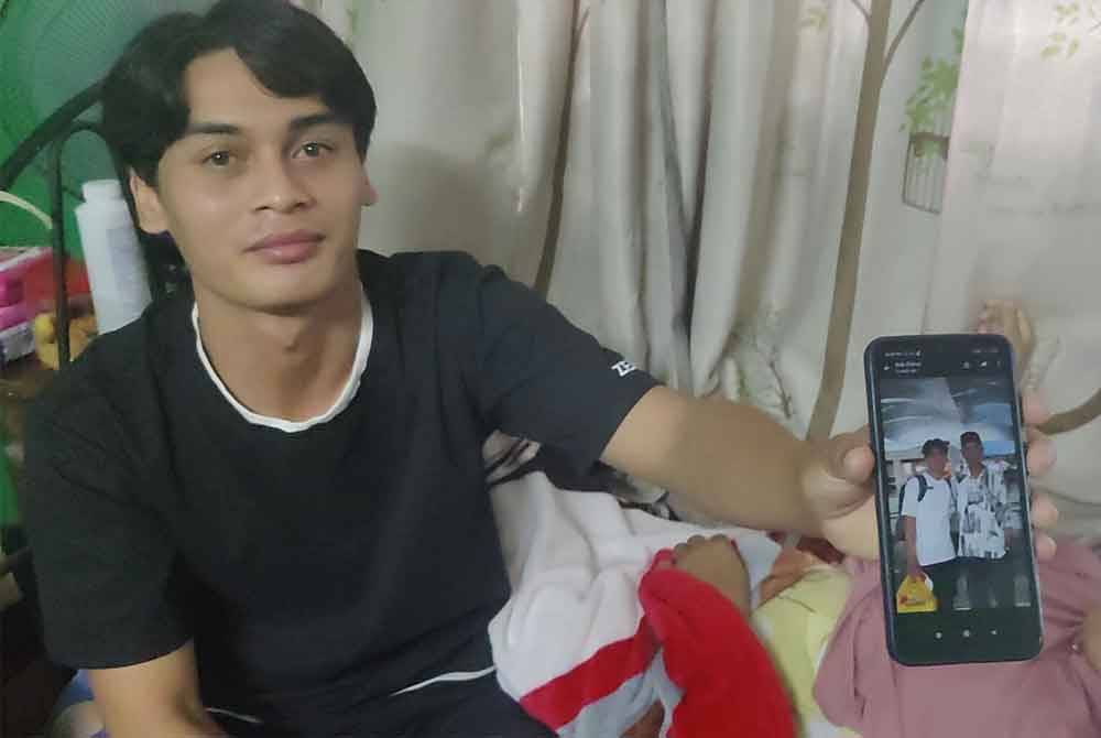 Muhammad Sadam menunjukkan gambar bapanya sambil berada di sisi ibunya di Kampung Assam Jawa di sini pada Isnin.