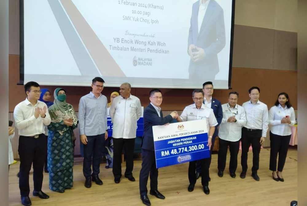 Kah Woh (kiri) menyerahkan replika cek kepada Mohamad Fauzi ketika majlis Penyerahan Cek Cura Bantuan Awal Persekolahan Negeri Perak kepada semua PPD di Sekolah Menengah Kebangsaan Yuk Choy di sini pada Khamis.