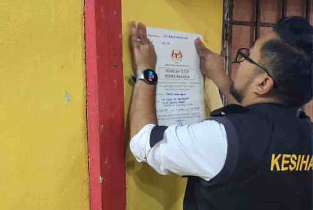 Anggota penguat kuasa JKNP menampal notis arahan tutup ke atas salah satu premis makanan yang kotor.