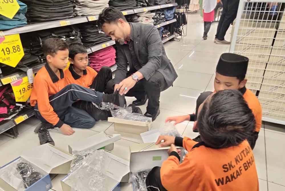 Norlisan (tengah) cuba memakaikan kasut kepada murid SK Kutan yang pada Program Tanggungjawab Sosial Korporat (CSR) ATH Group bersama Mydin di pasar raya itu.