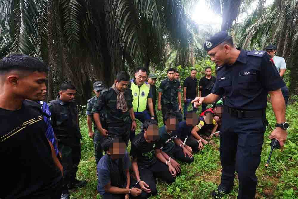 Mohd Naim (kanan) memeriksa tujuh tahanan warga Rohingya yang berjaya diberkas di sebuah ladang sawit di Jalan Kanchu, Tapah pada Rabu.