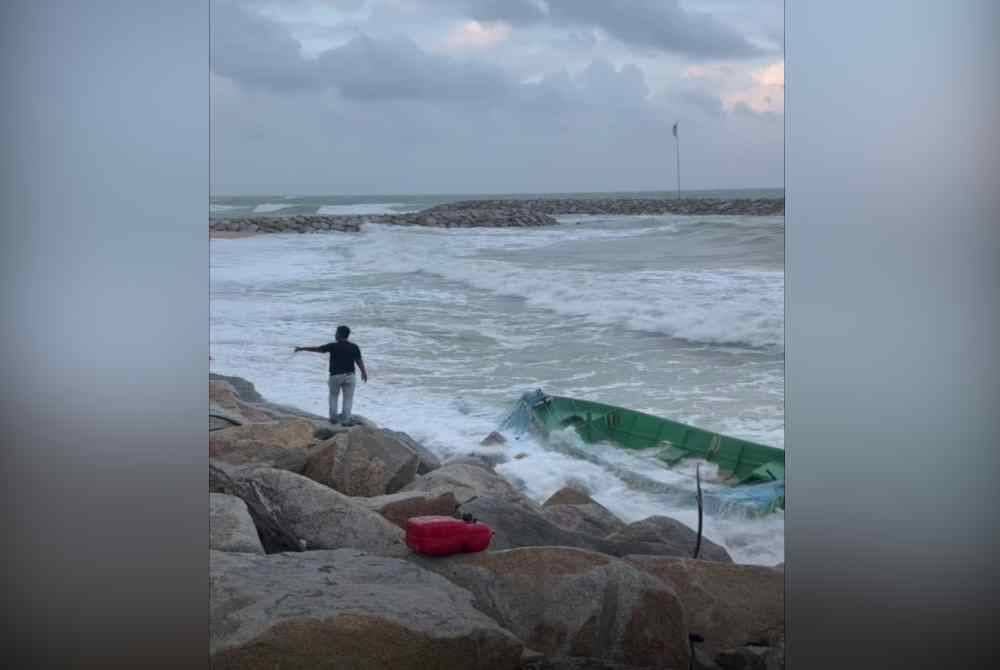 Tangkap layar video memaparkan bot nelayan yang tersadai di tepi pantai selepas terbalik kerana dilambung ombak dalam kejadian yang dipercayai berlaku pada Isnin.