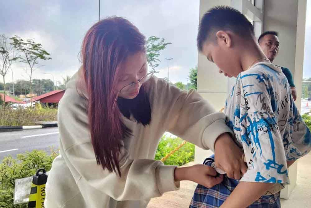 Kakak Koh Ming Zhe, Koh Pei Yee, 20 (kiri) membetulkan kain pelikat adiknya sebelum dikhatankan pada Program Khatan Perdana Hospital Tanah Merah.