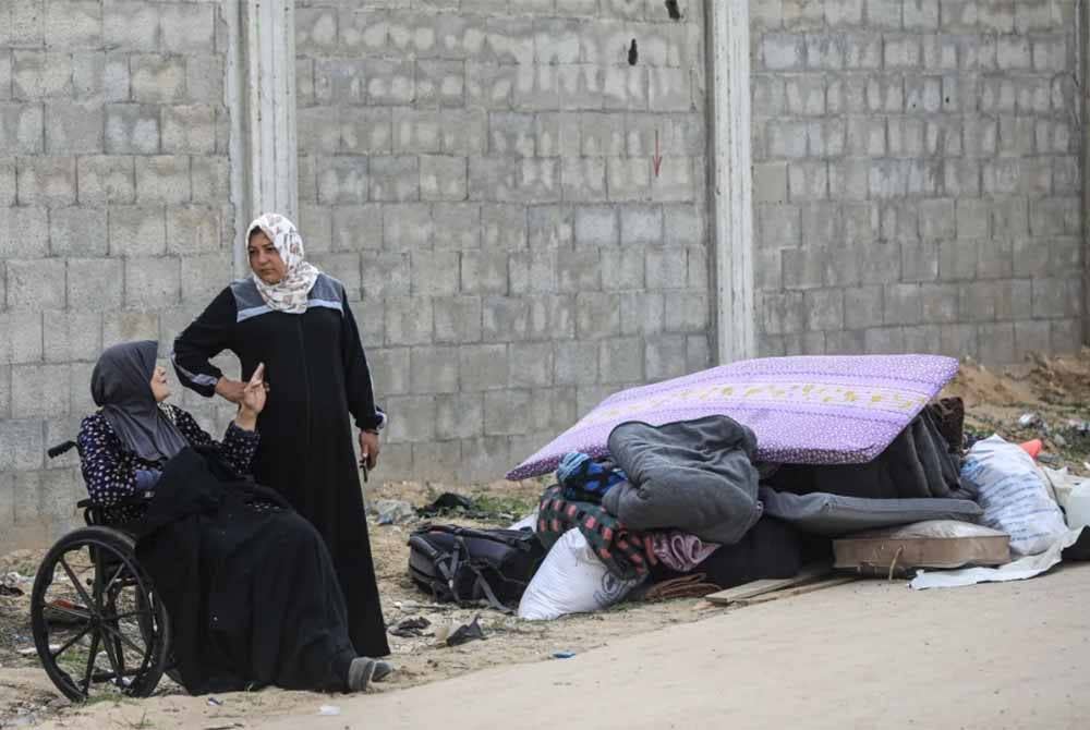 Dua wanita bersama barangan milik mereka yang terpaksa diletakkan di tepi jalan.