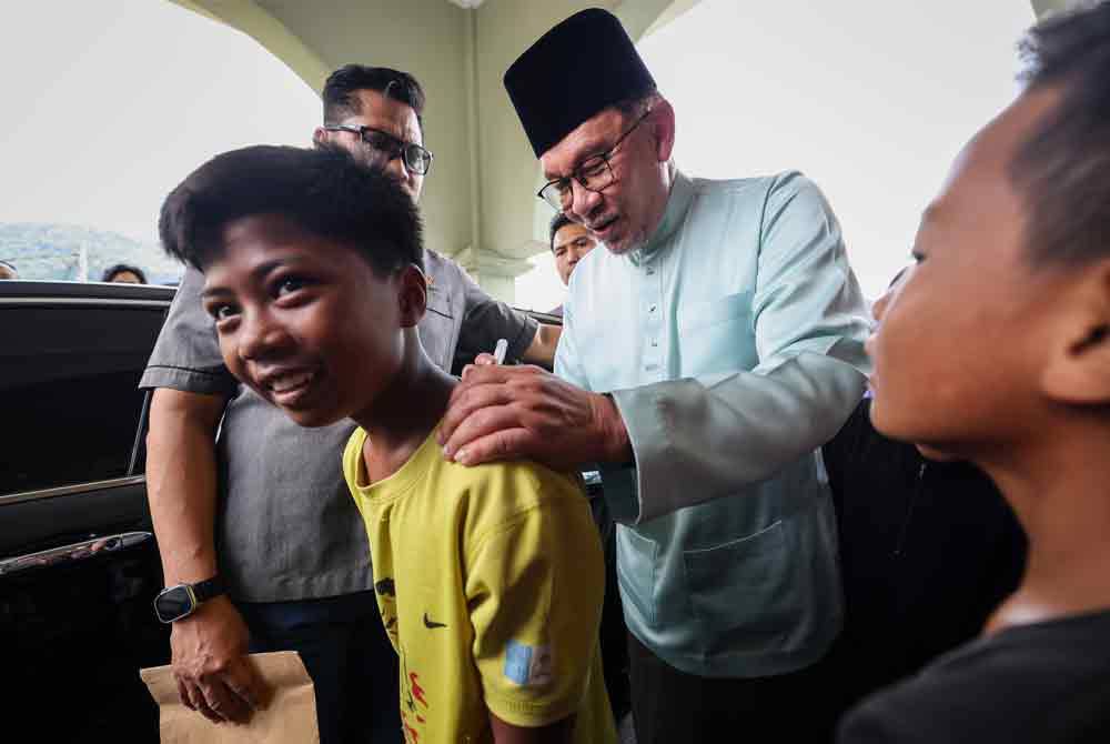 Anwar menandatangani baju seorang kanak-kanak selepas menunaikan solat Jumaat di Masjid Jamek Tengah Berapit. Foto Bernama