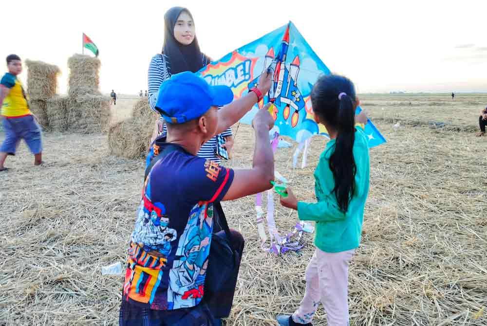 Mohd Fikry menunjukkan cara menaikkan wau kepada anaknya sambil ditemani isterinya di Kampung Benua pada petang Khamis.