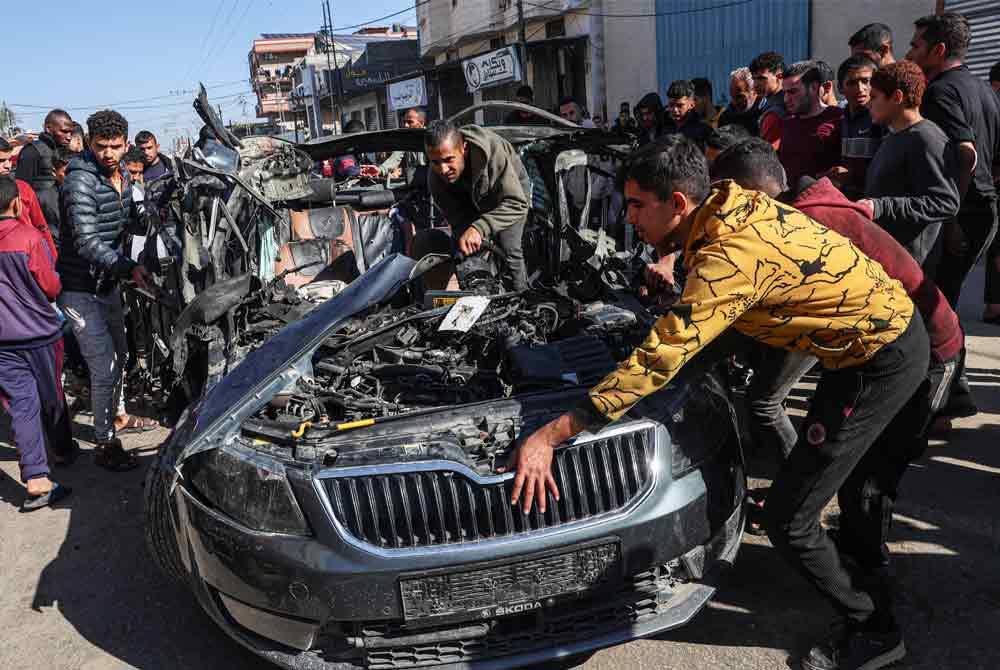 Orang ramai memeriksa kereta dua wartawan yang terkorban selepas tentera Israel mensasarkan mereka dalam serangan udara di Rafah. - AFP