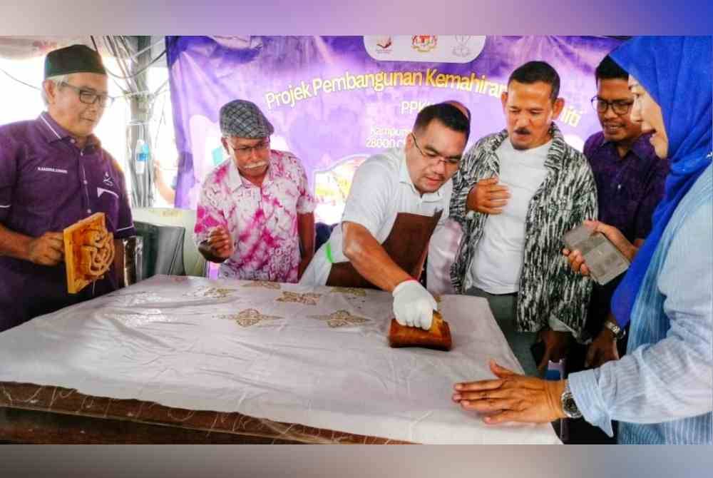 Amizar(tiga dari kiri) tidak melepaskan peluang mencuba menekap batik yang menjadi antara produk dipamerkan kepada pengunjung sempena Moh Karnival Makmur di Dataran Indera Pahlawan Chenor pada Sabtu.