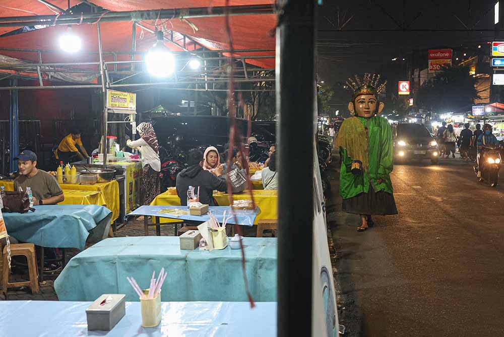 Penghibur jalanan mengenakan kostum gergasi yang dikenali sebagai Ondel-Ondel berjalan mengelilingi kawasan tumpuan bagi menghiburkan orang ramai dengan tarian mengikut alunan muzik yang dimainkan menerusi pembesar suara bersaiz mini ketika tinjauan di sekitar ibu kota Jakarta baru-baru ini. - Foto Bernama