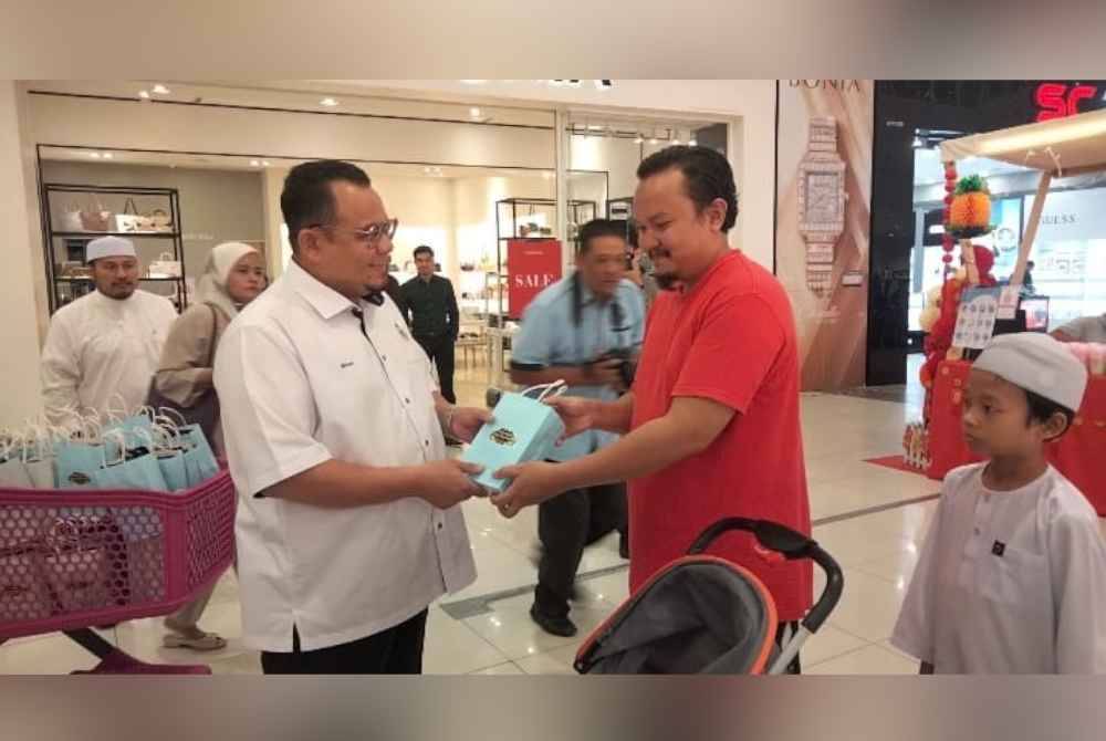 Hilmi (kiri) mengagihkan beg pakai buang kepada pelanggan Pasaraya Aeon Mall sempena Majlis Pelancaran Kota Bharu Bebas Beg Plastik pada Isnin.