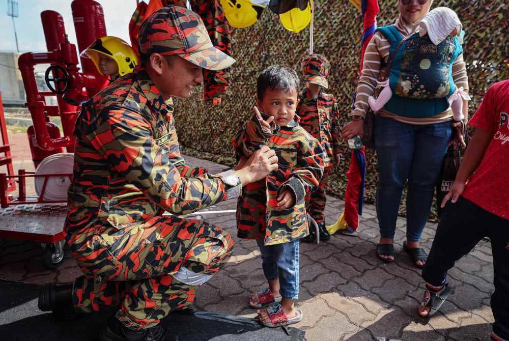 Anggota bomba menyarungkan pakaian seragam JBPM kepada peminat cilik. Foto Bernama