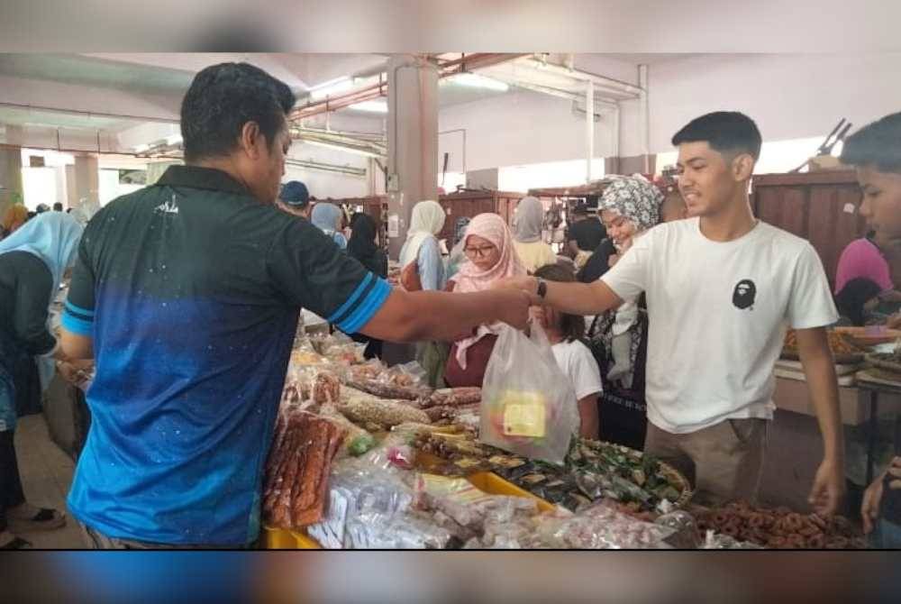 Mokhtar melayan pelanggan yang membeli makanan kering di gerainya di Pasar Siti Khadijah