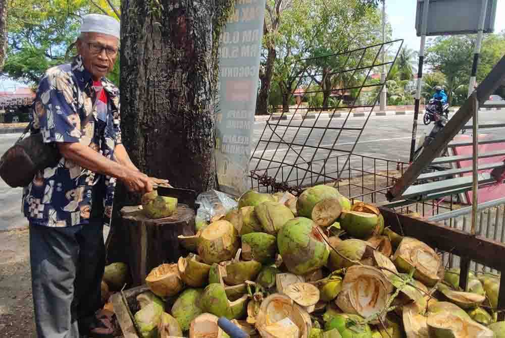 Hamid membelah kelapa untuk dijual kepada pelanggan di gerainya berhampiran Shahab Perdana, di sini.