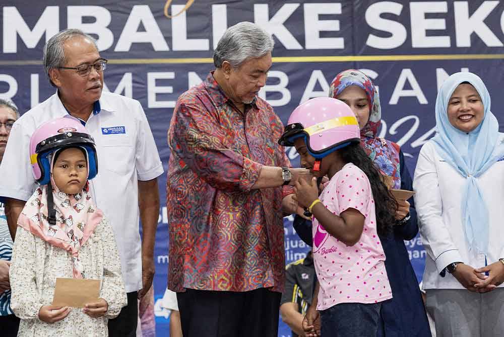 Ahmad Zahid memakaikan topi keledar kepada penerima sumbangan ketika hadir ke Majlis Penyampaian Sumbangan Kembali Ke Sekolah Parlimen Kawasan Bagan Datuk Tahun 2024 Kompleks UMNO Bagan Datuk hari ini. Foto Bernama