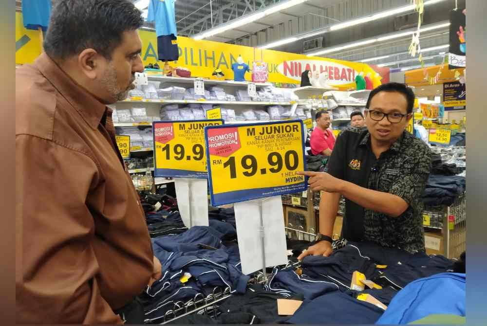 Kamalludin (kanan) menunjukkan harga beg sekolah yang ditawarkan selepas melancarkan Program Jualan Ihsan Rahmah Kembali Ke Sekolah di Pasar Raya Besar Mydin Meru di sini pada Rabu.