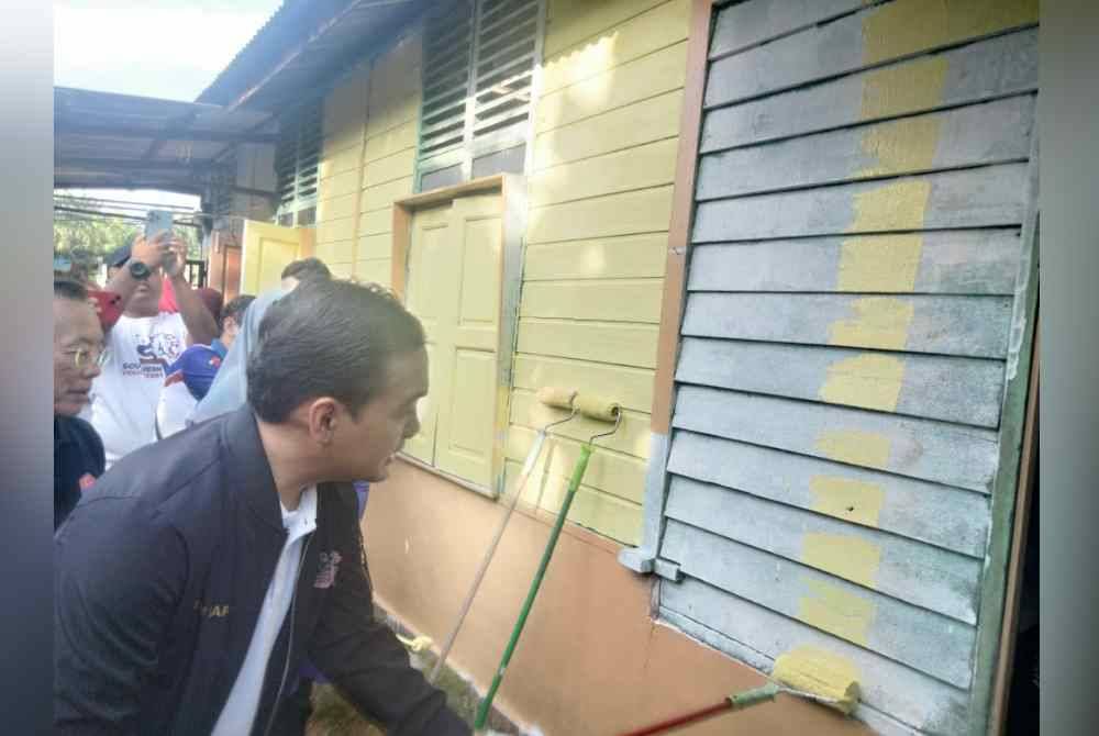 Onn Hafiz mengecat rumah penerima bantuan baik pulih rumah di Kampung Sungai Kuali, Serkat pada Ahad.