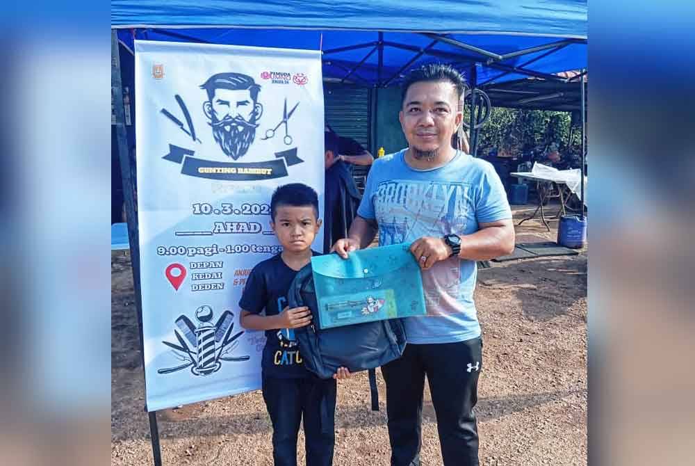 Mohd Firdaus menyerahkan set alat tulis kepada peserta terawal pada program gunting rambut percuma di Jengka.
