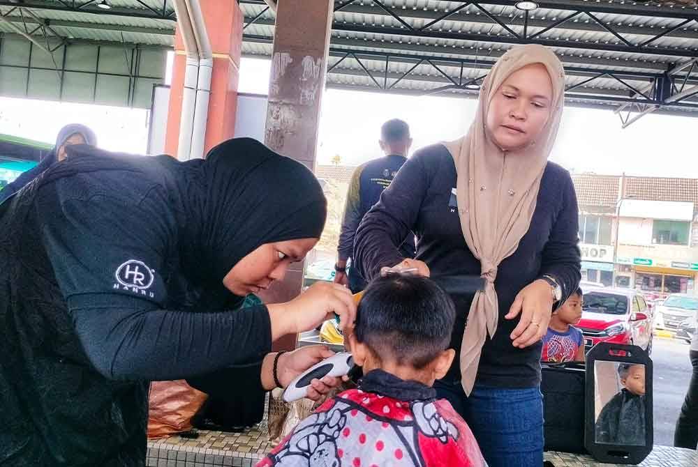 Hanis (kanan) ketika membantu perantis menggunting rambut peserta