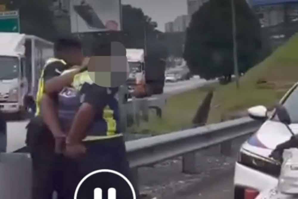 Tangkap layar video tular memaparkan seorang individu berpakaian uniform Polis Diraja Malaysia (PDRM) ditahan dua anggota polis berdekatan Plaza Tol Duta, di sini.