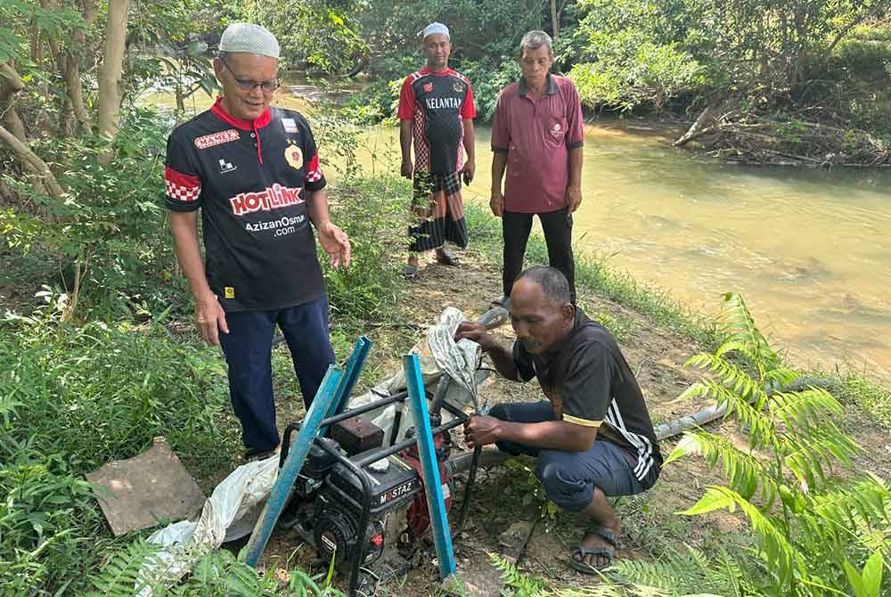 Mukhtar (kanan) dan beberapa penduduk melihat pam enjin yang diletakkan di tebing sungai untuk menyedut air.