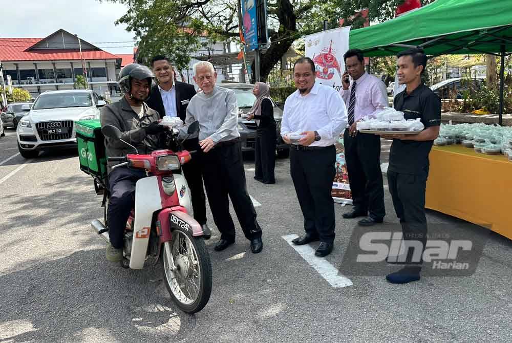 Kamarudin (tengah) mengagihkan bubur pulut hitam di Kota Bharu.