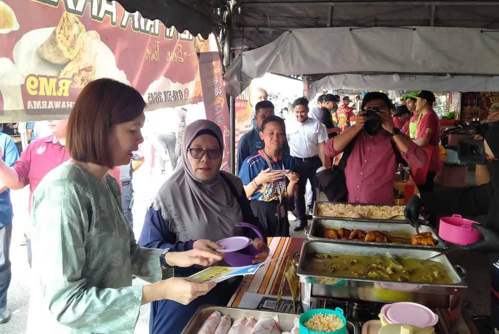 Sandrea (kiri) menyerahkan risalah mengenai kempen bawa bekal sendiri kepada pengunjung.