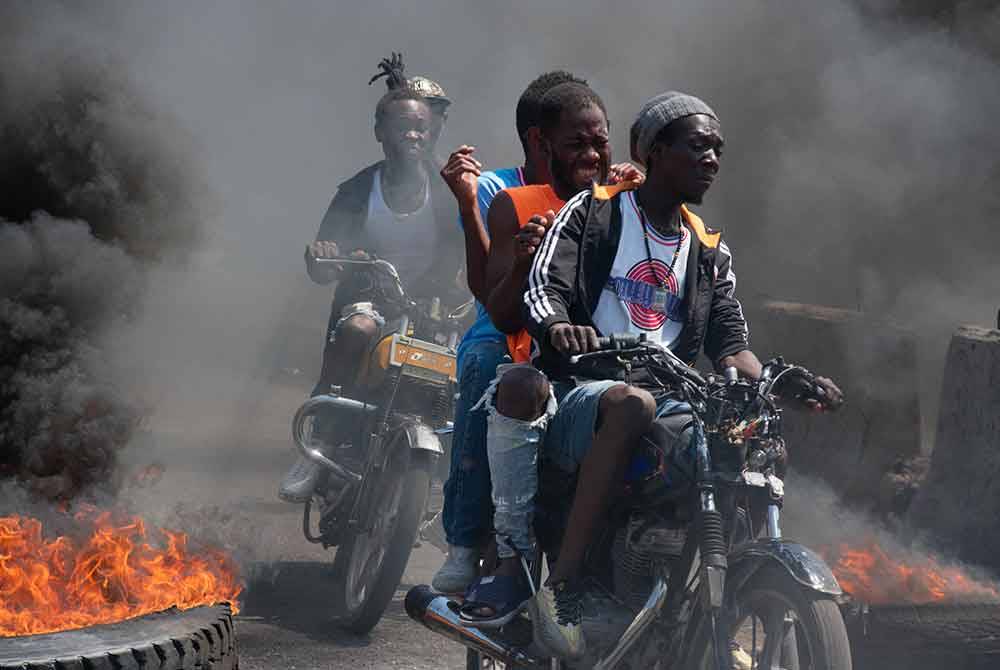 Beberapa pemuda Haiti menaiki motosikal melepasi jalan utama di Port-au-Princeyang ketika demonstrasi berlaku.