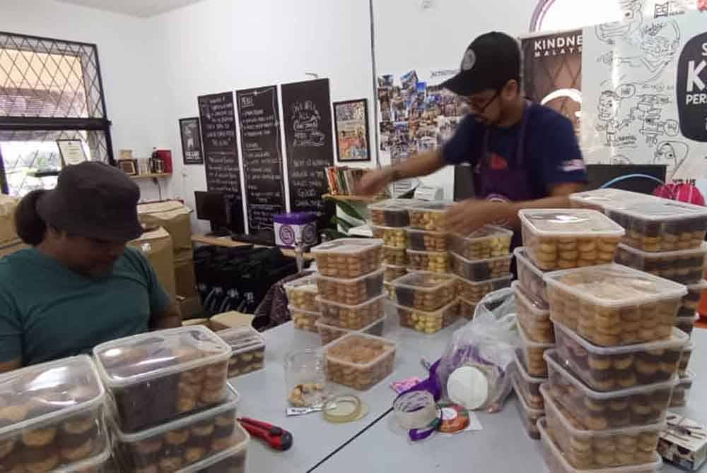 Mohd Azrul (kanan) menyusun kuih raya untuk diberikan kepada orang awam bersempena Aidilfitri tidak lama nanti.