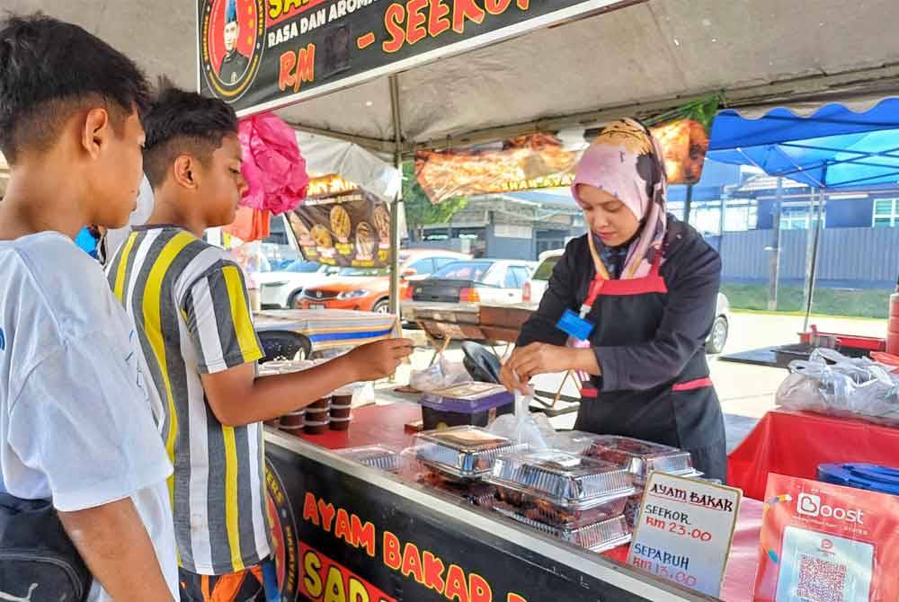 Pekerja kepada Siti Sarah melayan pelanggan di gerainya di bazar Ramadan Sungai Isap pada Sabtu.