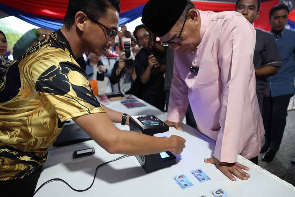 Saifuddin (tengah) melihat demonstrasi proses imbasan kad pengenalan pada program Mekar di Masjid An-Nur pada Jumaat.