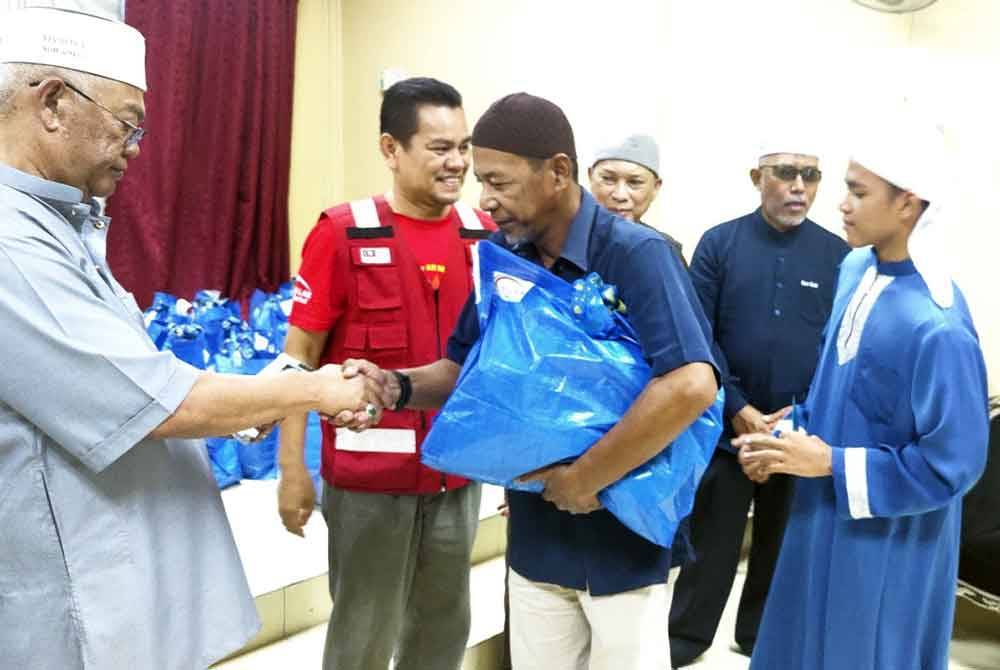 Noh (kiri) menyampaikan sumbangan kepada salah seorang penerima pada Majlis Penyampaian Sumbangan Salam Relief di Madrasah Tahfiz Haji Omar di Kampung Pinang Sungai Burung di sini pada Sabtu