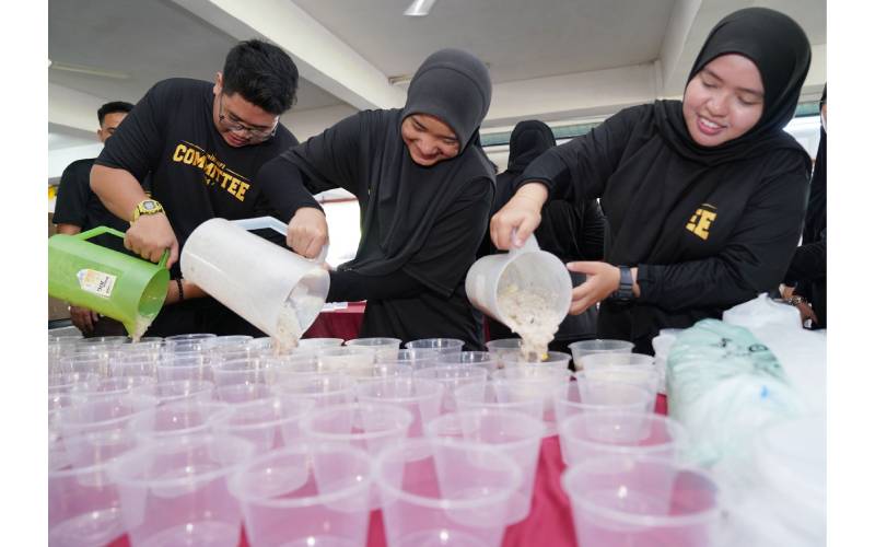 Para pelajar bertungkus lumus membungkus bubur lambuk yang siap dimasak untuk diagihkan kepada komuniti setempat.