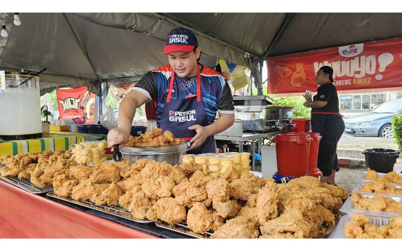 Peniaga ayam goreng yang lengkap memakai topi dan apron Petrol Gasul menyusun juadah jualannya di bazar Ramadan Stadium Perak di Ipoh.