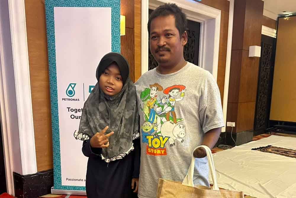 Mohd Nor Eizan (kanan) bersama Puteri Qurratul Ain (kiri) semasa menerima sumbangan daripada Yayasan Petronas.