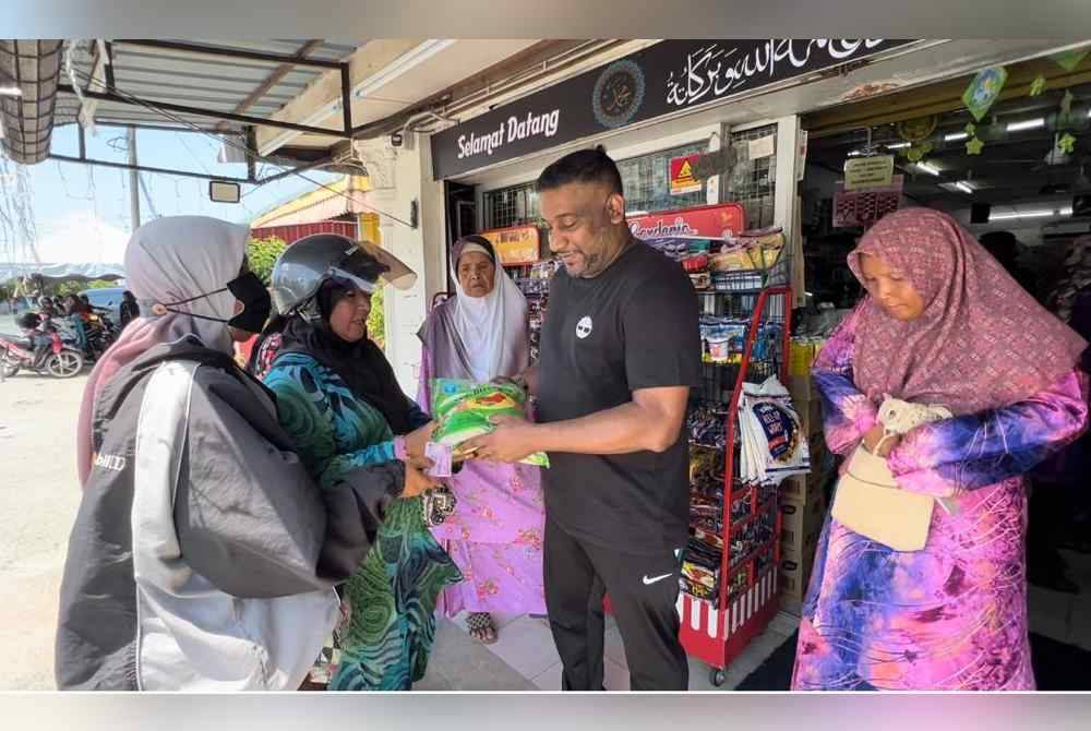 Abang Siti Fatimah, Mohd Ramlan (dua dari kanan) mengagihkan beras tambahan kepada mereka yang tidak sempat mendapatkan beras percuma di kedai runcit Gemilang Speed Mart di Kuala Terengganu pada Khamis.