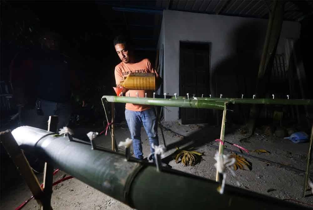 Mohd Amini menunjukkan cara pengisian minyak bagi nyalaan sumbu panjut buluh.