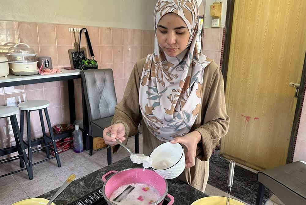 Nur Nadira memasukkan isi kelapa ke dalam kuah santan Bua Loy yang dihasilkannya.
