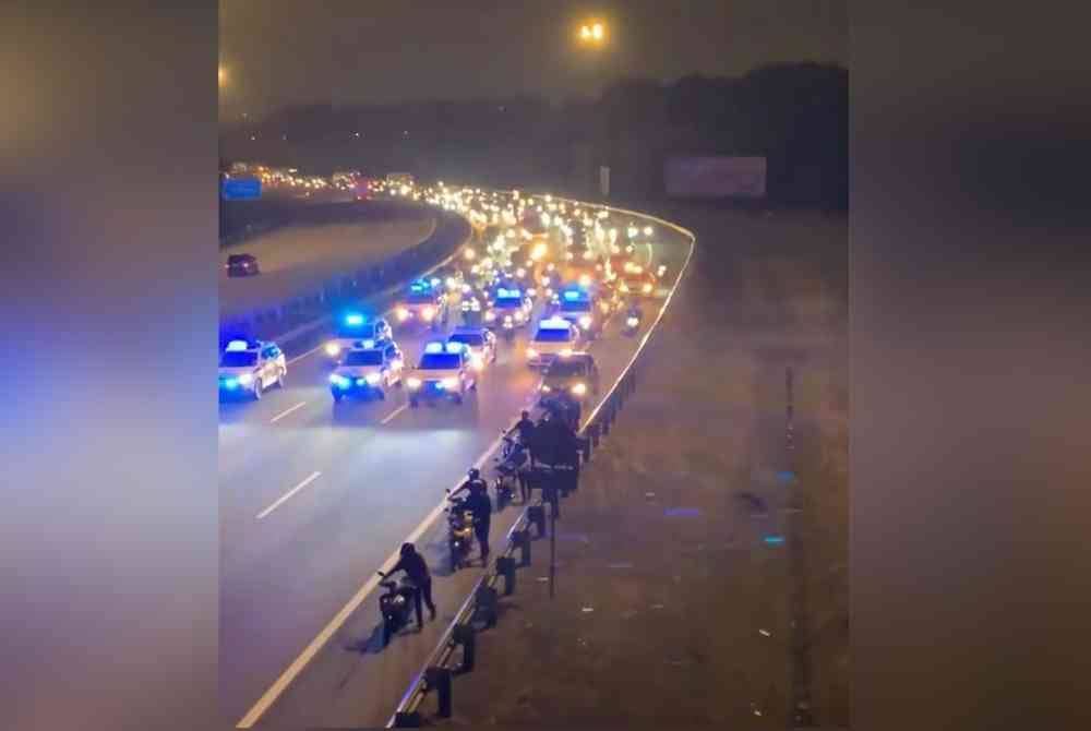 Tangkap layar video tular yang menyaksikan sekumpulan lelaki mengusung motosikal mereka dan diiringi kereta peronda polis.