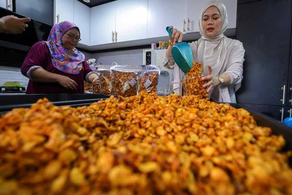 Nurul Arfiqah (kanan) memasukkan kudapan pedas berasaskan emping jagung ke dalam balang. Foto Bernama