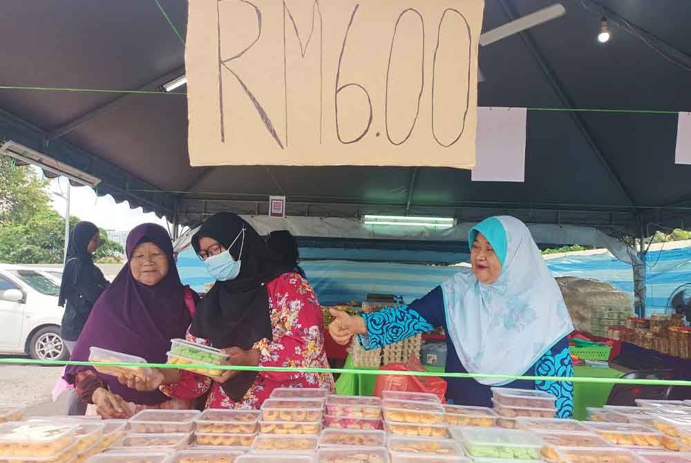 Suhairah (kanan) melayani pelanggan yang datang memilih biskut raya RM6 yang dijual di gerainya di lot parkir Stesen Minyak Shell di Jalan Hospital, Ipoh sempena Aidilfitri ini.