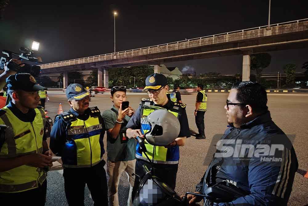 Azrin menyerahkan topi keledar percuma kepada penunggang motosikal sebagai kempen advokasi bagi menggantikan topi keledar yang rosak atau tidak ikut spesifikasi.