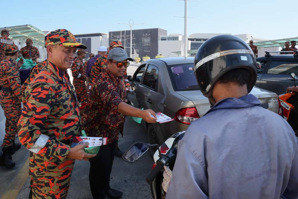 Hassan 'As'ari Omar (kiri) mengedarkan risalah keselamatan kebakaran sempena pelancaran Ops Siaga Raya dan Kempen Keselamatan Kebakaran di Jambatan Angkat Kuala Terengganu hari ini. Foto Bernama
